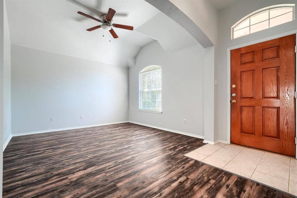 Vaulted ceiling featuring a ceiling fan, wood-finish flooring, arched window with blinds, panel-style entry door, and tile flooring