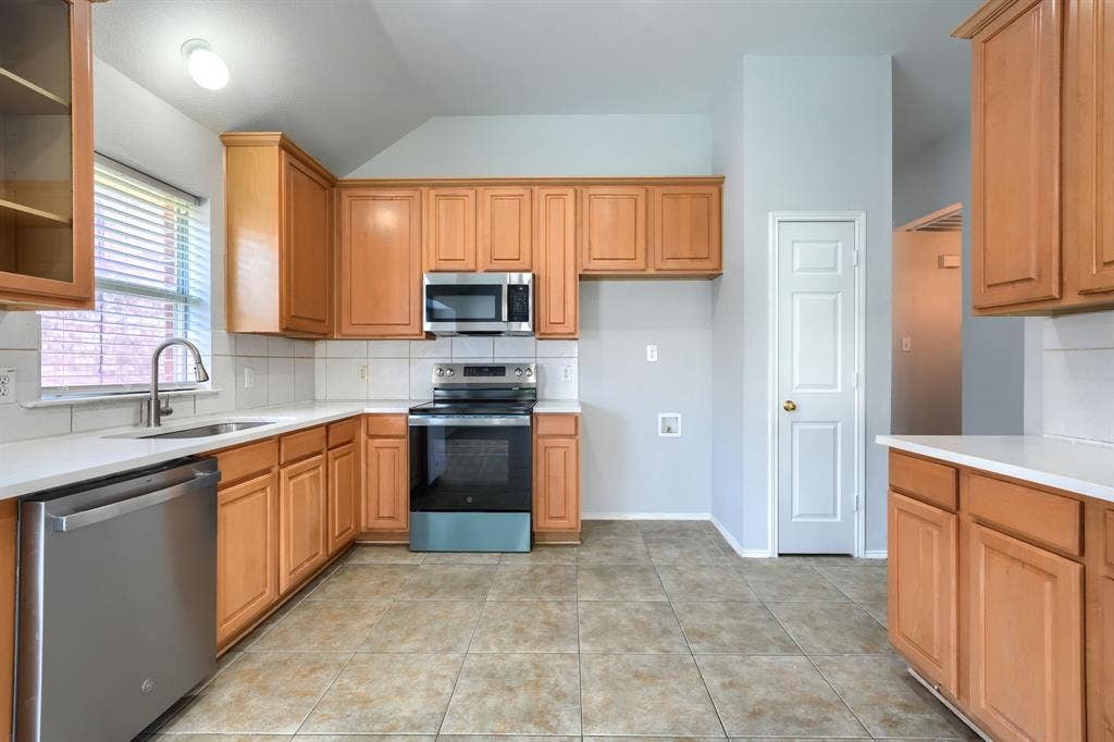 Kitchen featuring wood cabinetry, stainless steel appliances, white countertops, a tile backsplash, and tile flooring