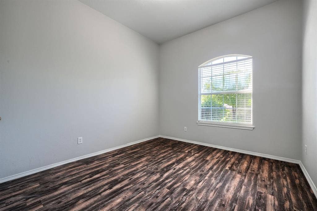 Arched window with blinds, wood-finish flooring, and light-toned walls