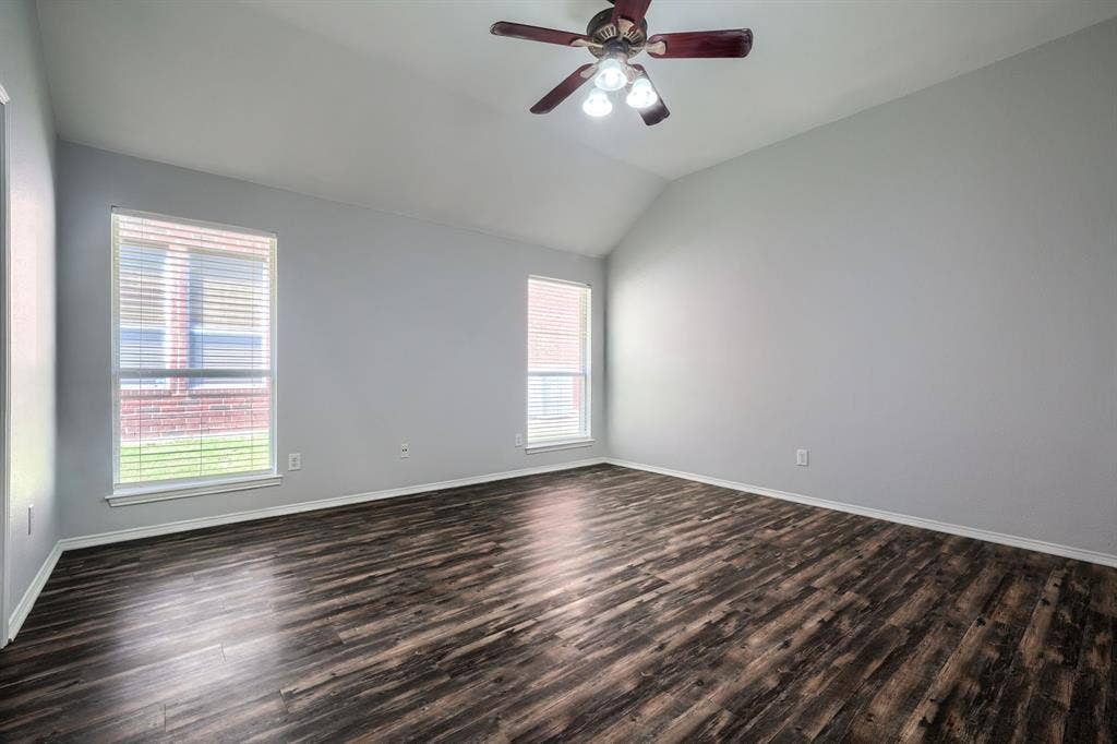 Vaulted ceiling featuring a ceiling fan with integrated lighting, two windows with blinds, and wood-finish flooring