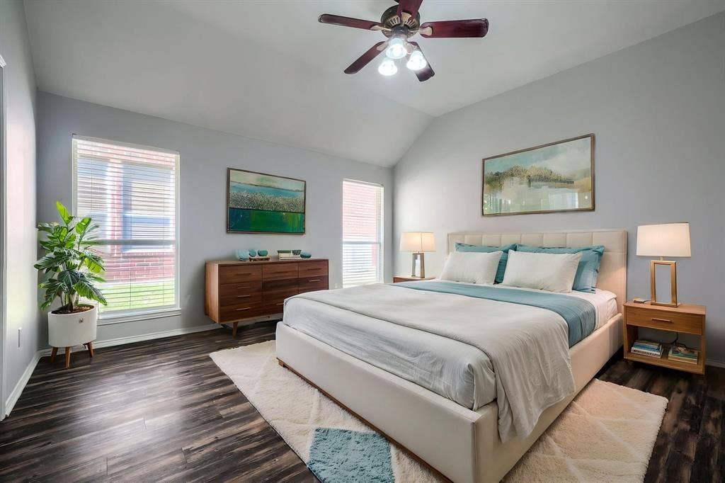 Vaulted ceiling with a ceiling fan, two windows with blinds, and dark wood-finish flooring