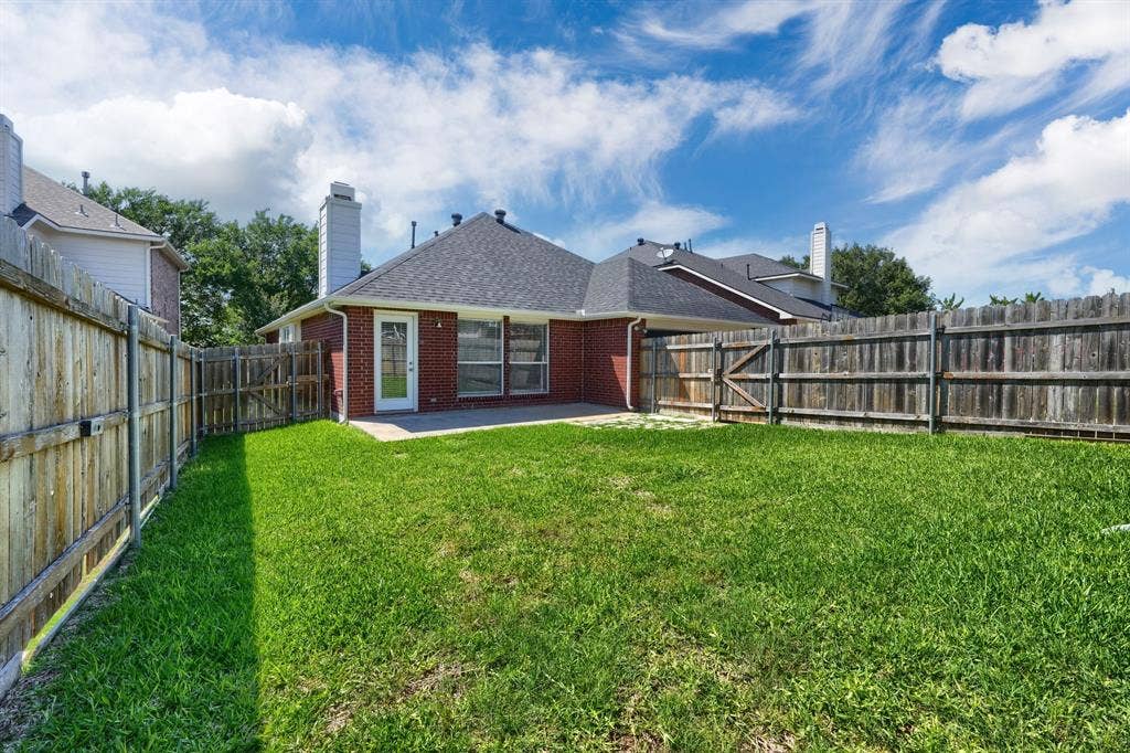 Expansive rear lawn with brick exterior, concrete patio, and a privacy fence