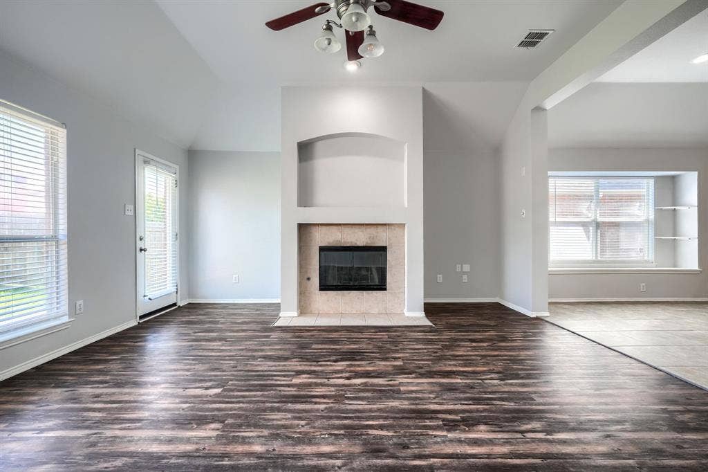 Spacious living area featuring wood-finish flooring, a ceiling fan with integrated lighting, and a tiled fireplace with an arched niche