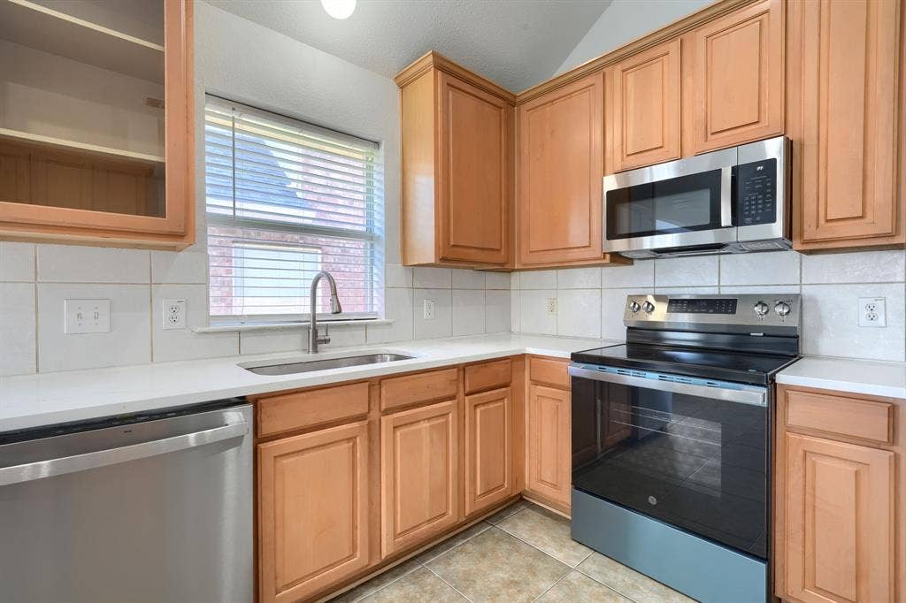 Kitchen featuring light wood cabinetry, a stainless steel dishwasher, a stainless steel electric range, a stainless steel microwave, and white countertops