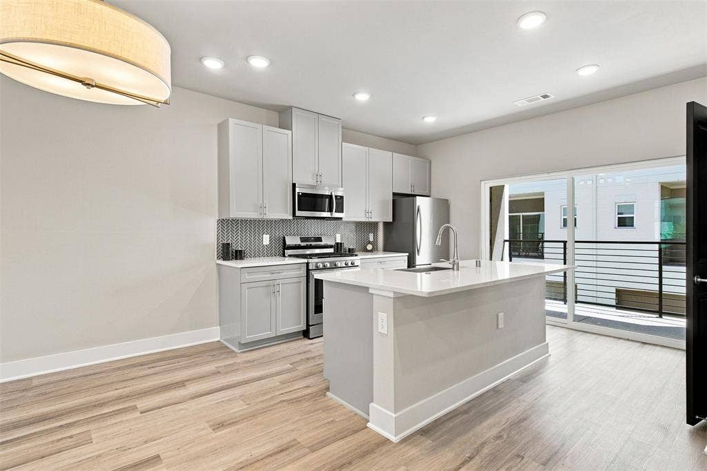 3352 Norris Street, Plano, TX 75074 Modern kitchen featuring stainless steel appliances, light gray cabinetry, and a white countertop island with an undermount sink