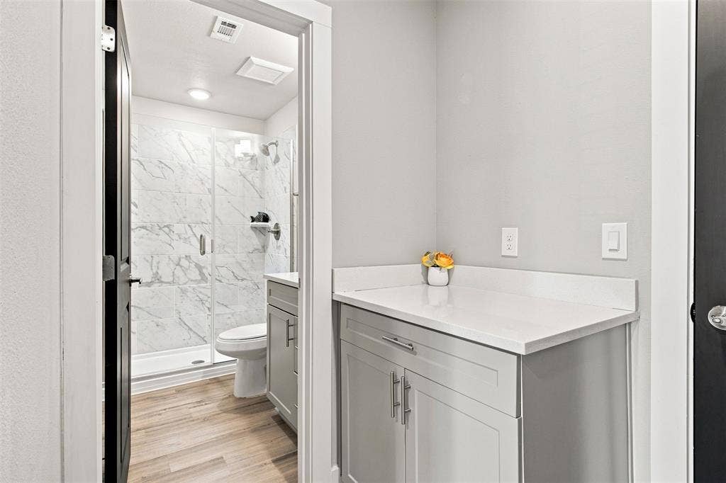 3352 Norris Street, Plano, TX 75074 White quartz countertop with shaker-style cabinetry, wood-finish flooring, and a walk-in shower with glass enclosure and marble-look tile