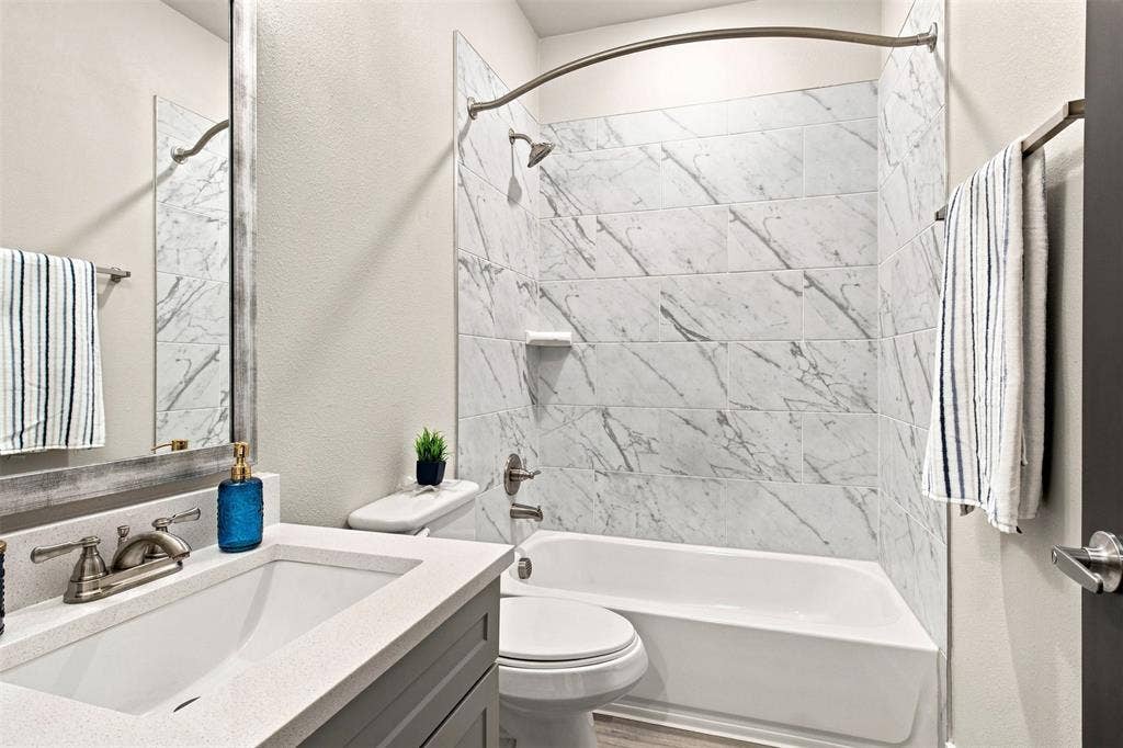 3352 Norris Street, Plano, TX 75074 Bathroom featuring a white vanity with an undermount sink, brushed nickel faucet, large framed mirror, and a tiled shower with a built-in shelf