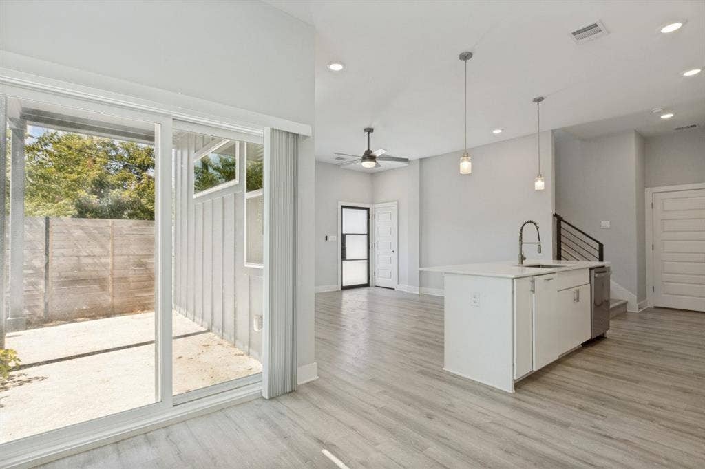 1042 Rosemont Street, #1, Austin, TX 78723 Open-concept living area featuring wood-finish flooring, recessed lighting, a kitchen island with an undermount sink and stainless steel dishwasher, and sliding glass doors opening to a private patio