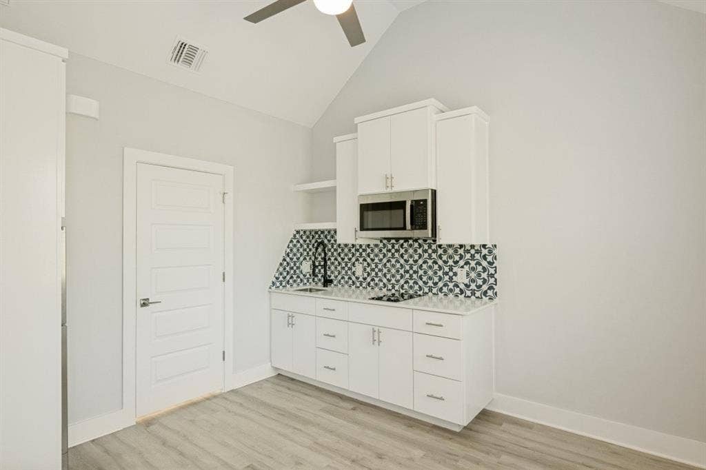 1042 Rosemont Street, #1, Austin, TX 78723 Vaulted ceiling with a ceiling fan, white paneled door, wood-finish flooring, built-in microwave, and patterned tile backsplash