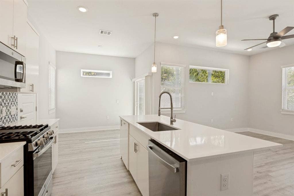1042 Rosemont Street, #1, Austin, TX 78723 Modern kitchen featuring white cabinetry, stainless steel appliances, a center island with sink, pendant lighting, and wood-finish flooring