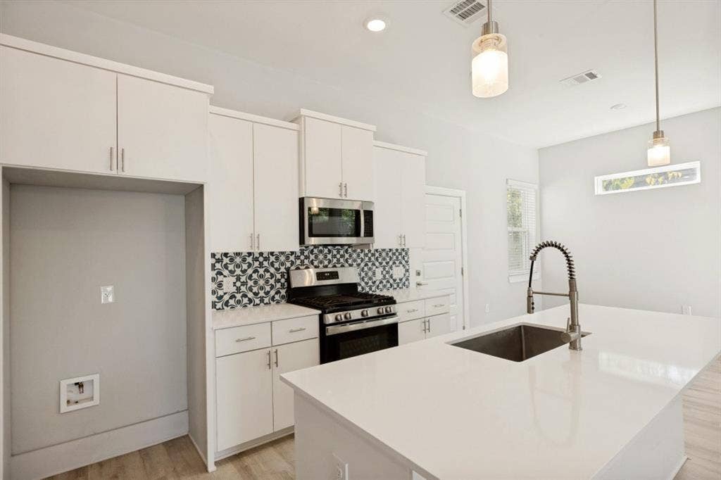 1042 Rosemont Street, #1, Austin, TX 78723 Modern kitchen featuring white cabinetry, stainless steel appliances, a patterned tile backsplash, a large island with an undermount sink, and wood-finish flooring
