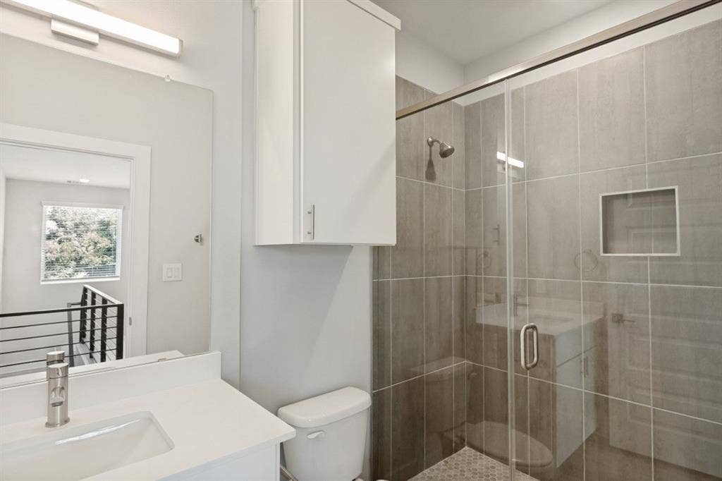 1042 Rosemont Street, #1, Austin, TX 78723 Bathroom featuring a frameless glass shower enclosure, a tiled shower surround with a built-in niche, and a white vanity with an integrated sink