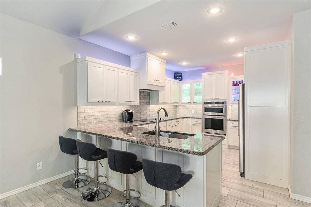 109 Briarwood Drive, Gun Barrel City, TX 75156 Modern kitchen featuring white shaker-style cabinetry, stainless steel appliances, subway tile backsplash, and a waterfall-edge island with dark granite countertops