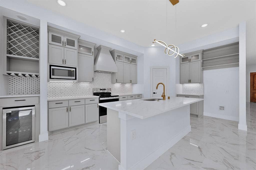 102 Redondo Drive, Gun Barrel City, TX 75156 Kitchen featuring a central island with an integrated sink, light-toned cabinetry, stainless steel appliances, a geometric tile backsplash, and polished tile flooring
