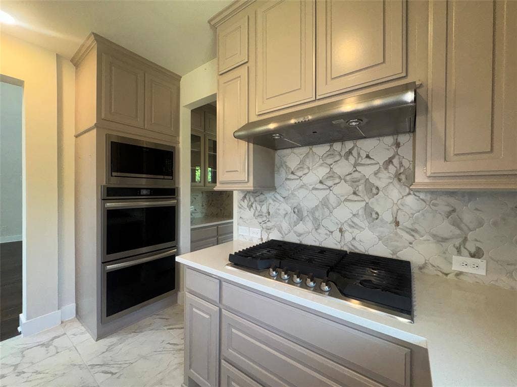1701 Shamrock Green, Mesquite, TX 75181 Light-toned cabinetry with crown molding, double wall ovens, integrated microwave, stainless steel range hood, and a decorative tile backsplash