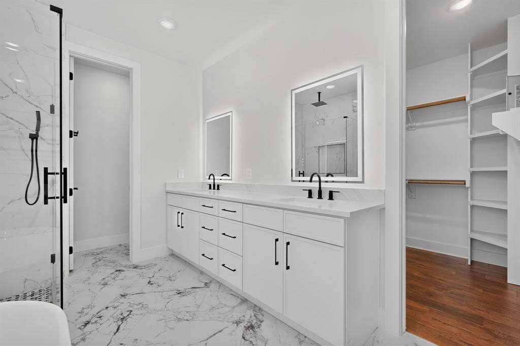1672 Brookview Drive, Lancaster, TX 75146 Dual vanity with white cabinetry and black hardware, stone countertops, two illuminated mirrors, walk-in shower with black-framed glass enclosure, and marble-look tile flooring