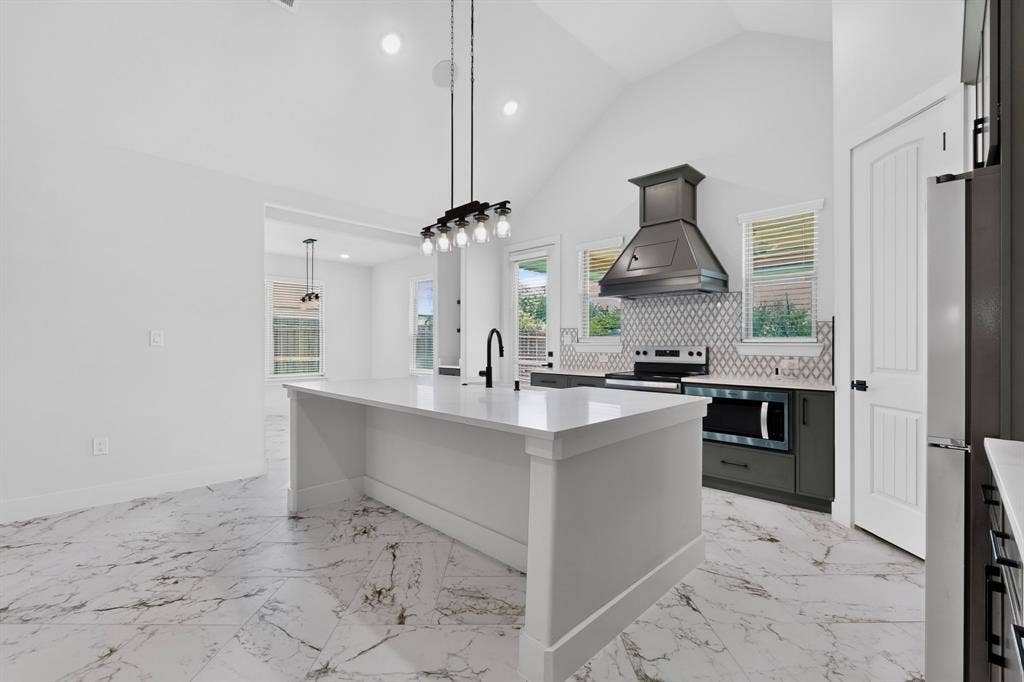 1672 Brookview Drive, Lancaster, TX 75146 Kitchen featuring a vaulted ceiling, large central island with a sink, stainless steel appliances, decorative range hood, and tile backsplash