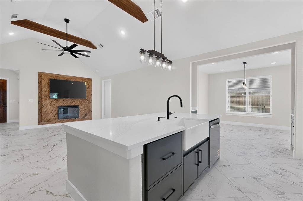 1672 Brookview Drive, Lancaster, TX 75146 Spacious kitchen island with a farmhouse sink and matte black faucet, integrated dishwasher, vaulted ceiling with exposed wood beams, and a modern ceiling fan