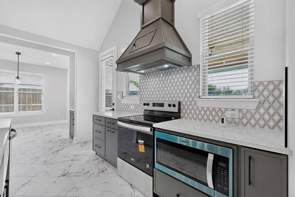 1672 Brookview Drive, Lancaster, TX 75146 Vaulted ceiling kitchen featuring stainless steel appliances, patterned tile backsplash, quartz countertops, and gray cabinetry
