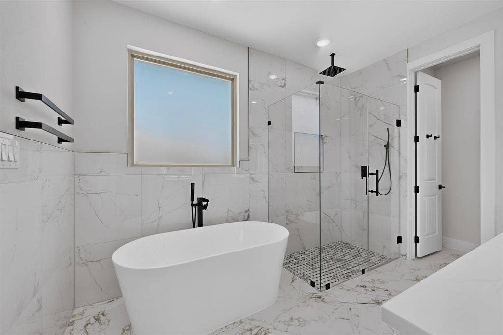 1672 Brookview Drive, Lancaster, TX 75146 Freestanding soaking tub with a floor-mounted faucet, walk-in glass shower enclosure, rainfall showerhead, and marble-look wall and floor tiling