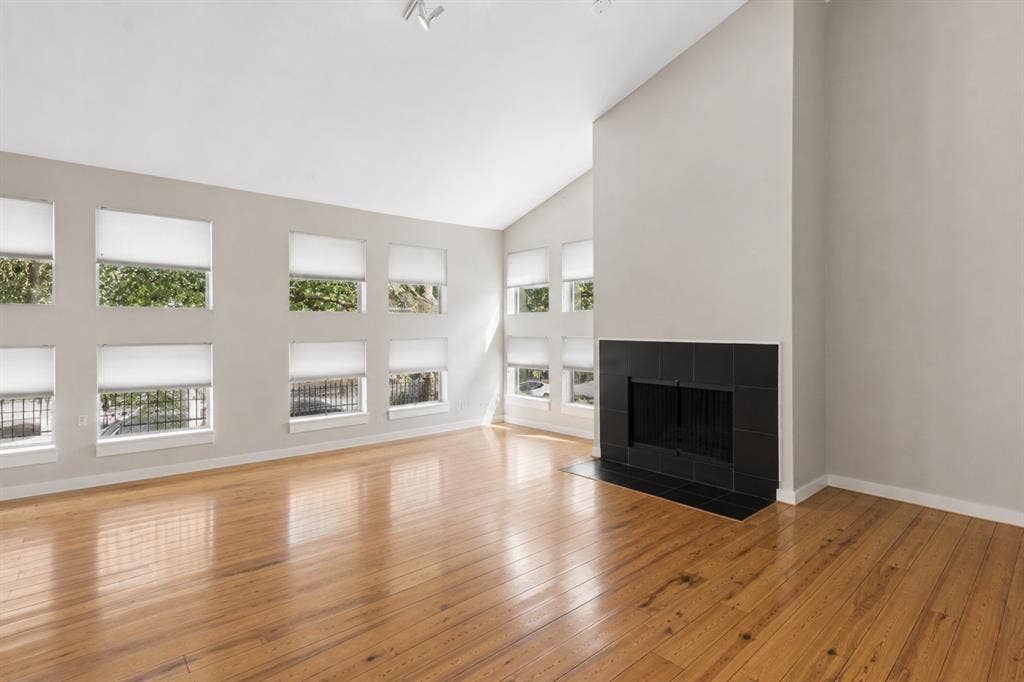 2714 Shelby Avenue, Dallas, TX 75219 Vaulted ceiling, multiple windows with roller shades, wood-finish flooring, and a black-tiled fireplace