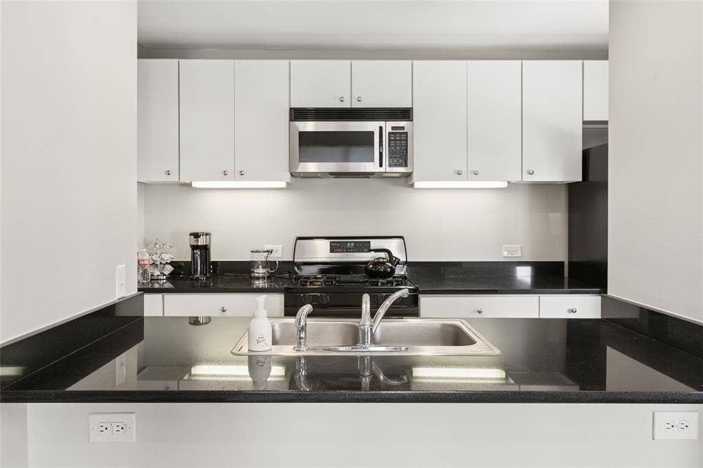2714 Shelby Avenue, Dallas, TX 75219 Kitchen featuring black countertops, stainless steel sink, gas range, microwave, and white cabinetry