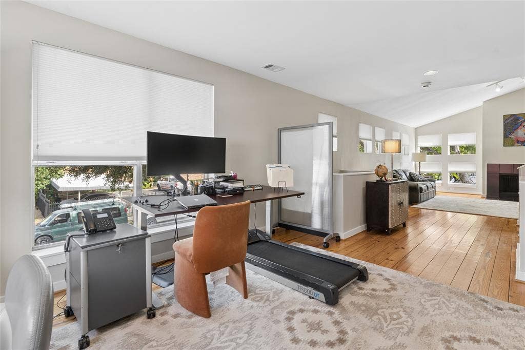 2714 Shelby Avenue, Dallas, TX 75219 Bright home office featuring warm wood-finish flooring, expansive desk workspace with built-in storage, large windows with motorized roller shades, and abundant natural light