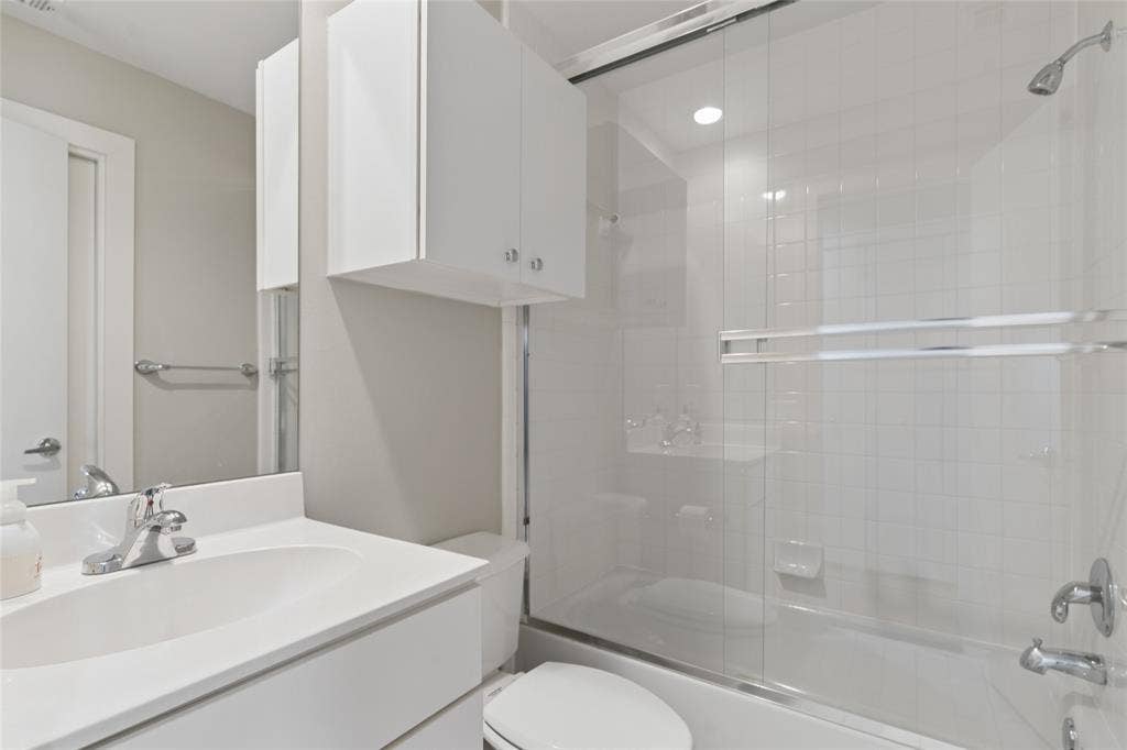 2714 Shelby Avenue, Dallas, TX 75219 Bathroom featuring a vanity with an integrated sink, polished chrome faucet, white cabinetry, and a shower-tub combination with a sliding glass enclosure
