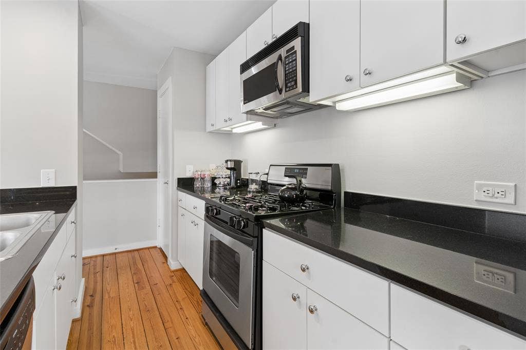 2714 Shelby Avenue, Dallas, TX 75219 Galley kitchen featuring wood-finish flooring, white cabinetry, dark countertops, a stainless steel gas range, and an over-the-range microwave