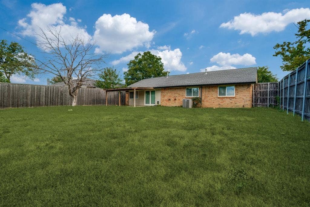 1412 E Park Boulevard, Plano, TX 75074 Expansive backyard featuring a manicured lawn, wood fencing, covered patio, and brick exterior