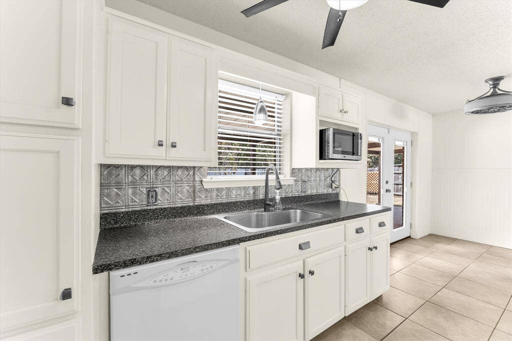 4626 Lexington Street, Bellmead, TX 76705 White cabinetry, dark stone-finish countertops, stainless steel sink, patterned tile backsplash, and light-toned tile flooring