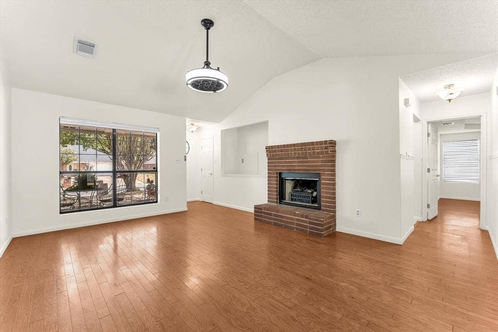 4626 Lexington Street, Bellmead, TX 76705 Vaulted ceiling, wood-finish flooring, brick fireplace, large window, and ceiling-mounted light fixture