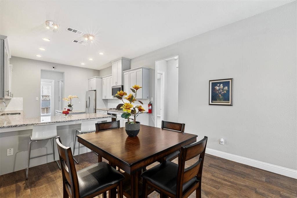 8226 Natchez Trail, Dallas, TX 75252 Open-concept kitchen and dining area featuring light-toned cabinetry, stainless steel appliances, and a breakfast bar with stone-finish countertops