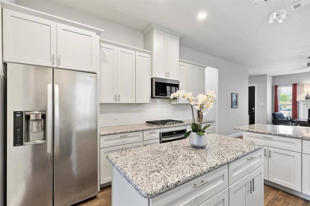 8226 Natchez Trail, Dallas, TX 75252 Kitchen featuring white cabinetry, stainless steel appliances, speckled stone countertops, a tile backsplash, and wood-finish flooring