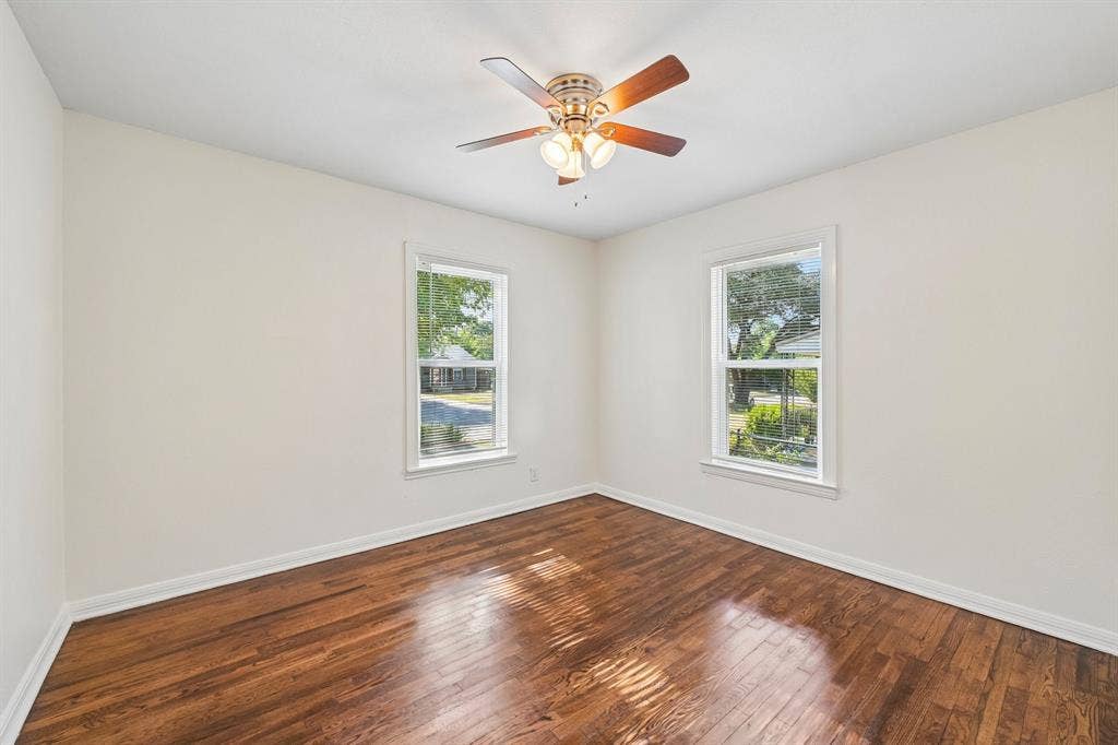 5012 Pamela Drive, Fort Worth, TX 76116 White walls with wood-finish flooring, two large windows, and a ceiling fan with integrated lighting