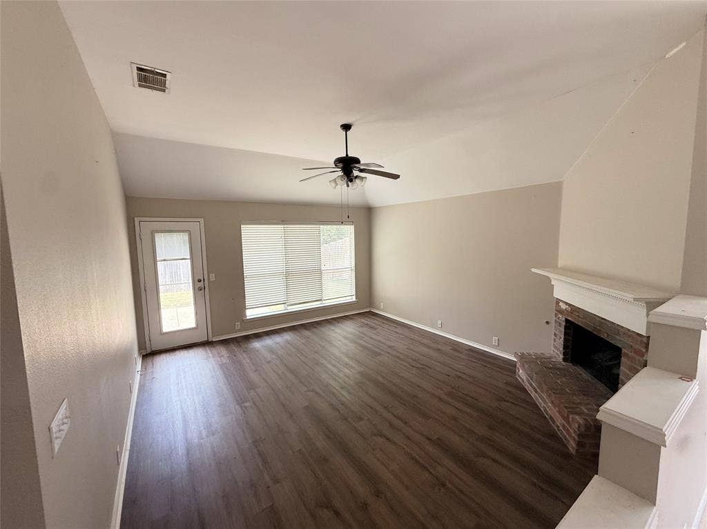 Vaulted ceilings, wood-finish flooring, corner brick fireplace with mantel, ceiling fan, and large windows with blinds