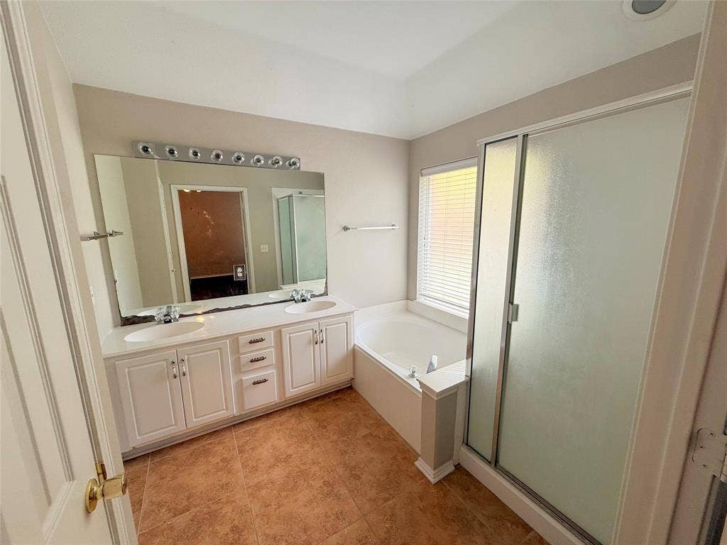 Dual vanity with white cabinetry and integrated sinks, a built-in soaking tub, a separate shower enclosure with frosted glass, and tile flooring