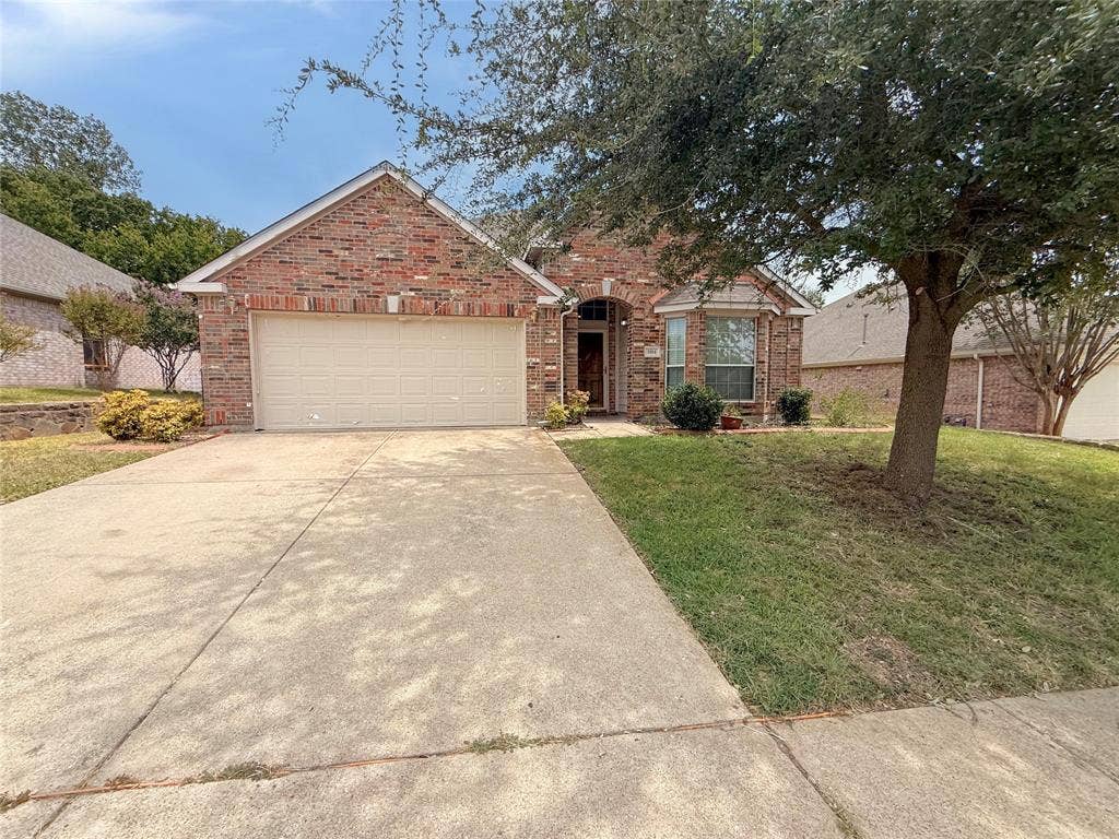 Brick exterior with an integrated garage, concrete driveway, and mature landscaping
