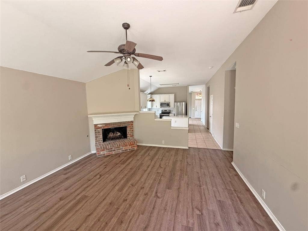 Spacious living area featuring wood-finish flooring, a brick fireplace with a white mantel, and a ceiling fan