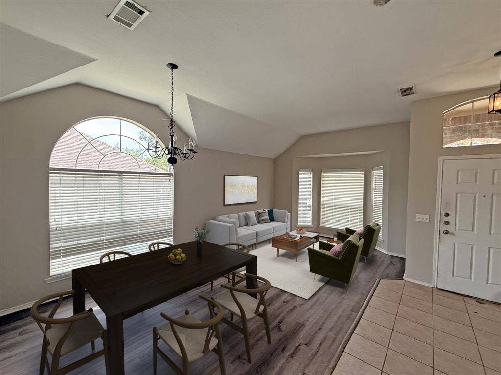 Vaulted ceilings, wood-finish flooring, a decorative chandelier, a large arched window, and a white paneled entry door