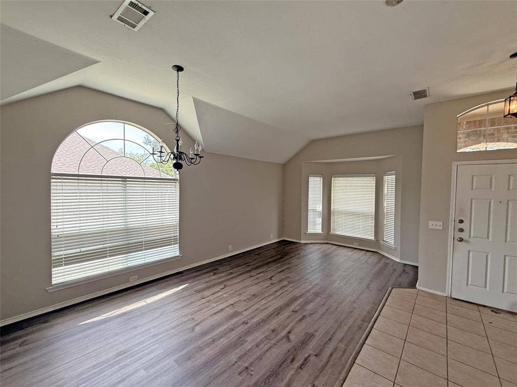 Vaulted ceiling with decorative chandelier, arched window, wood-finish flooring, bay window, and tile entryway