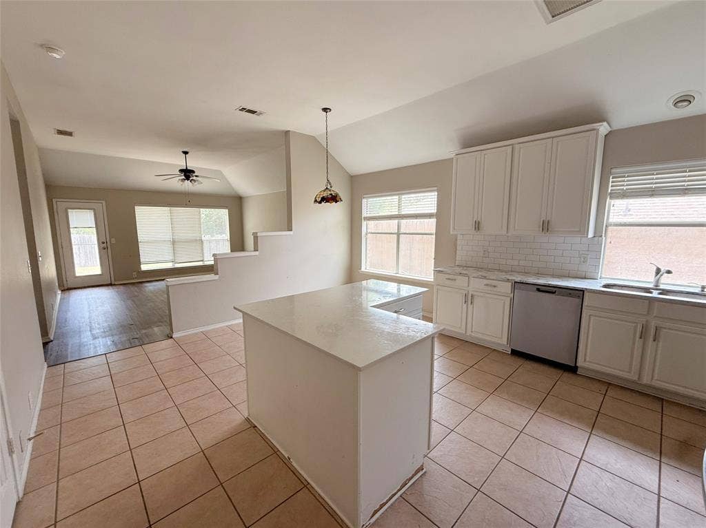 Kitchen featuring an island, white cabinetry with silver hardware, subway tile backsplash, and stainless steel dishwasher