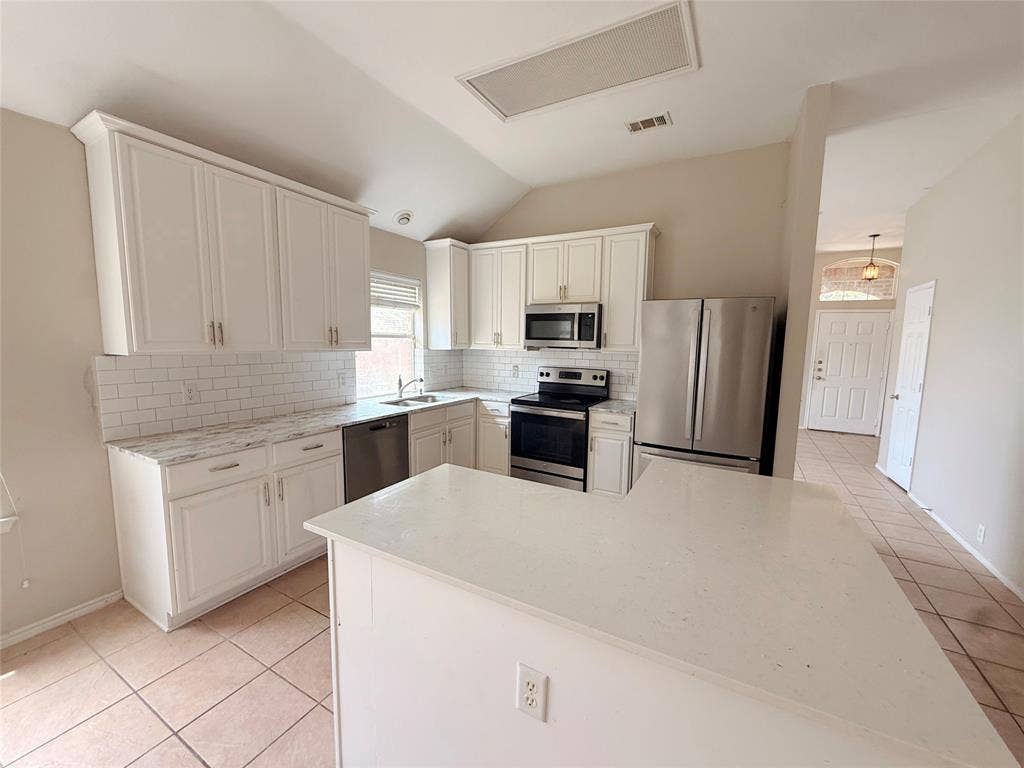 Kitchen featuring white cabinetry, subway tile backsplash, stainless steel appliances, and a central island with a solid surface countertop