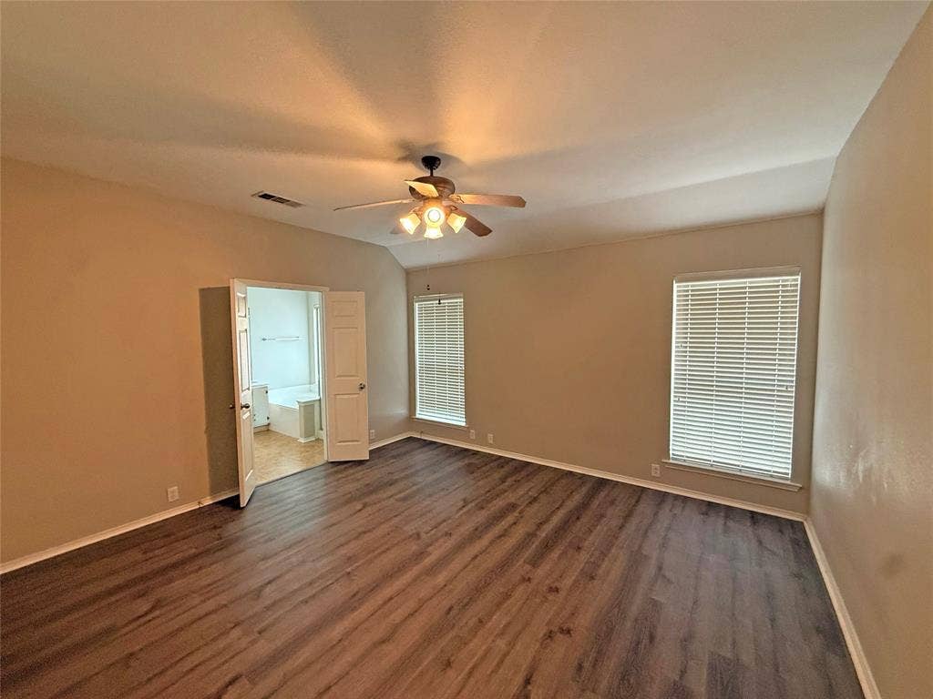 Spacious room with wood-finish flooring, vaulted ceiling, and two windows with blinds