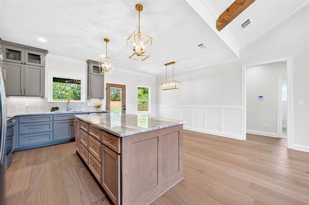 305 Grace Lane, Athens, TX 75751 Two-tone kitchen cabinetry, wood-finish flooring, gold-tone pendant lighting, exposed wood beam, and wainscoting details