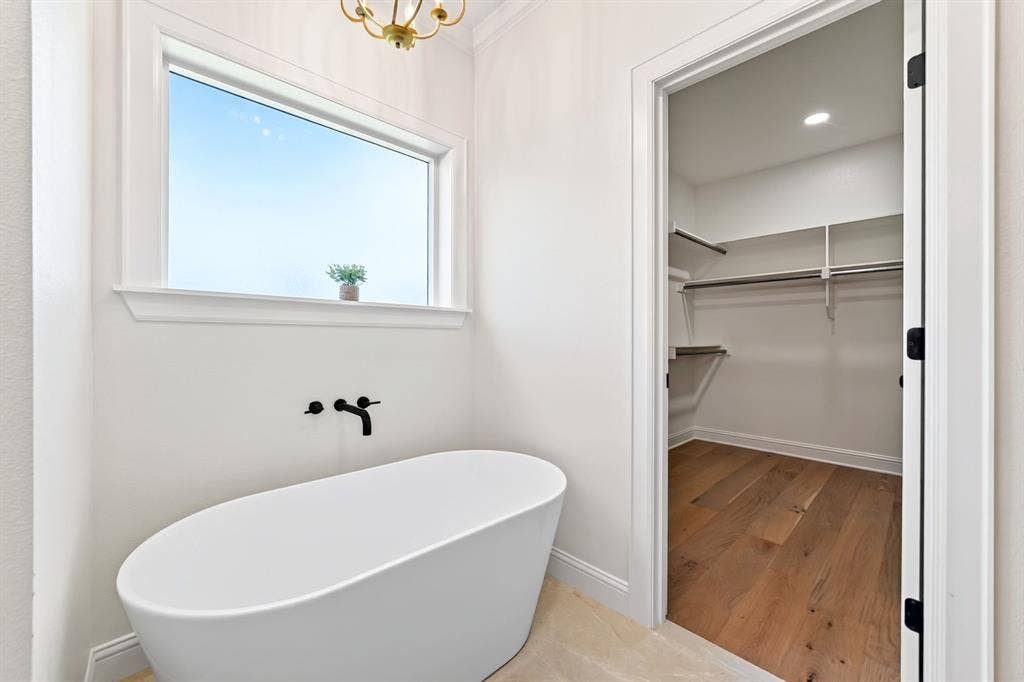 305 Grace Lane, Athens, TX 75751 Freestanding oval soaking tub with matte black wall-mounted faucet, large window, and light tile flooring