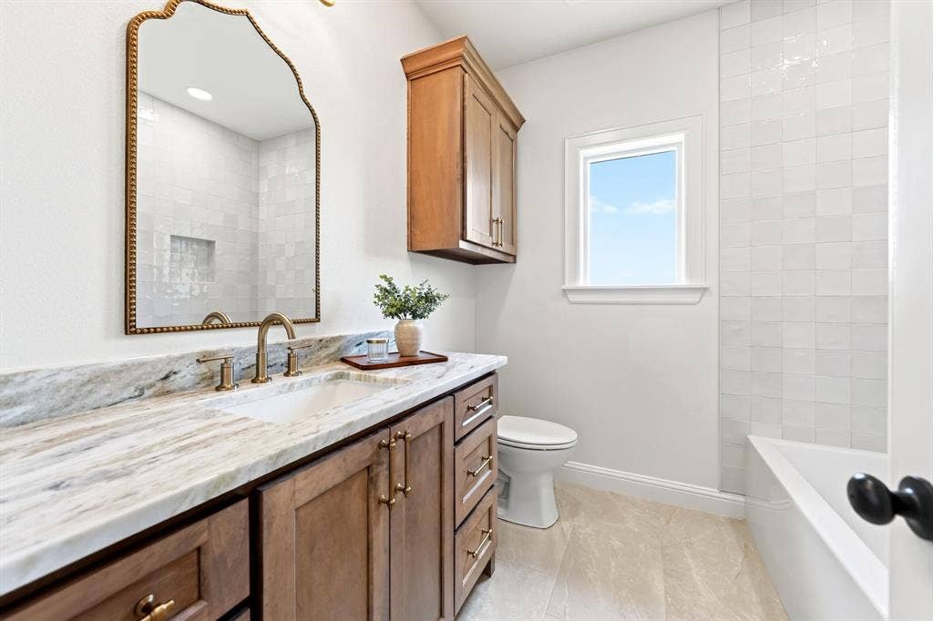 305 Grace Lane, Athens, TX 75751 Built-in vanity with wood cabinetry, light-toned stone countertop, brass-finish faucet, and an ornate mirror