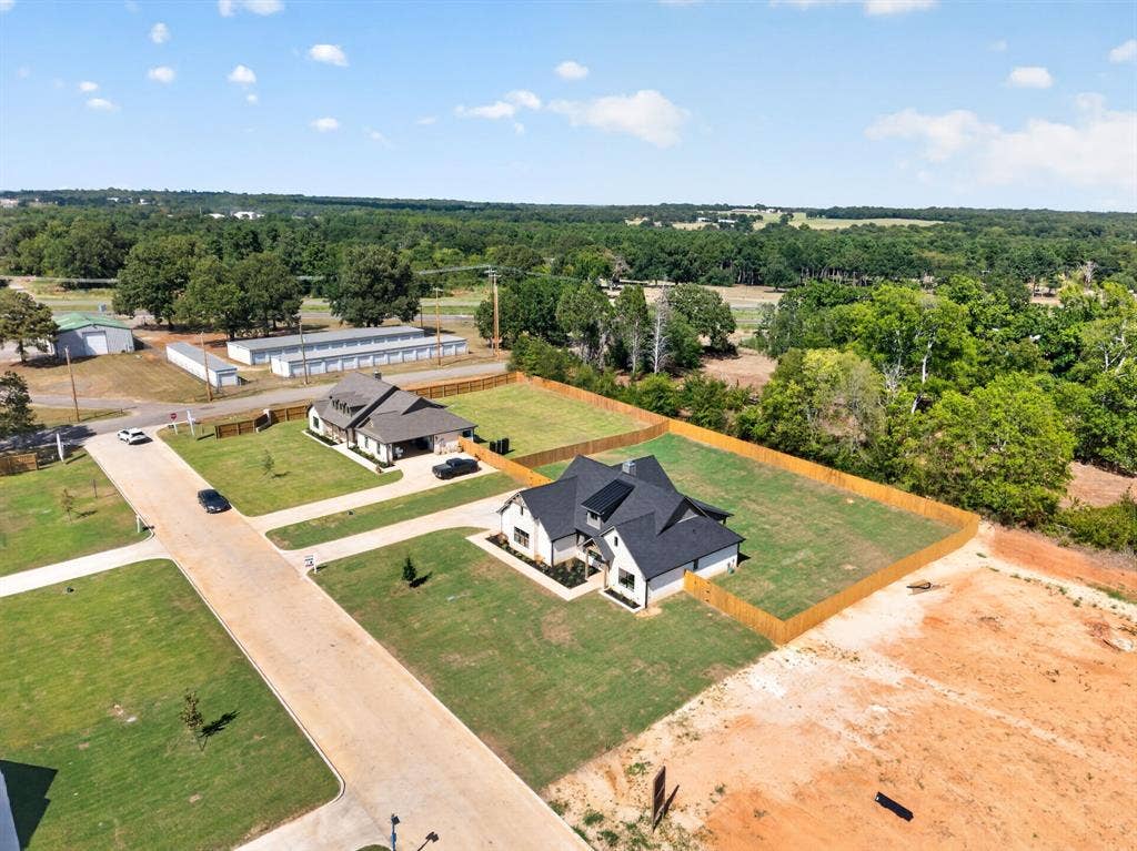 305 Grace Lane, Athens, TX 75751 Gabled roofline, light-colored exterior with dark trim, fenced property line, established residential street, and surrounding mature trees