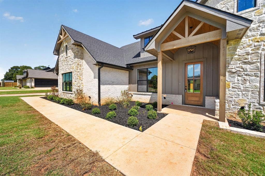 305 Grace Lane, Athens, TX 75751 Exterior featuring stone and painted brick siding, a gabled roofline, a covered entry with wood accents, and a natural wood-finish front door