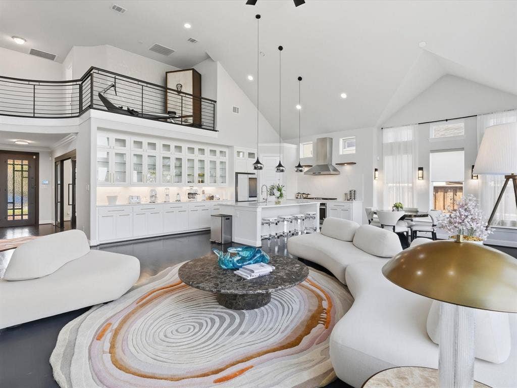 3505 Wycliff Avenue, McKinney, TX 75071 Vaulted ceilings, a second-story interior balcony with metal railing, an extensive built-in display cabinet with glass doors, a kitchen island with seating, and dark wood-finish flooring